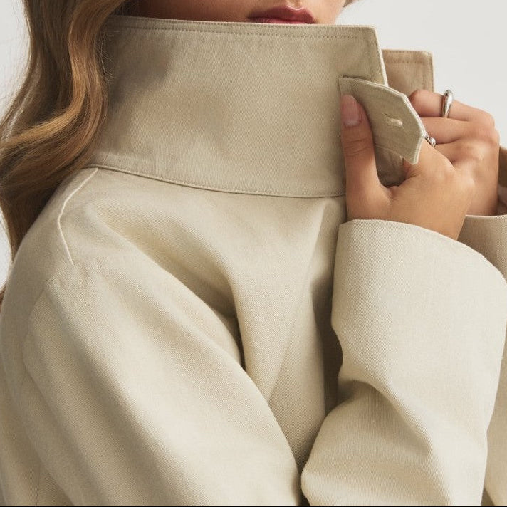 Stand-up collar of the Capsule Original Trench held closed at the neck